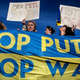 Protestors weep as they hold multiple posters and a banner reading "Stop Putin Stop War" while organizing in Rome,